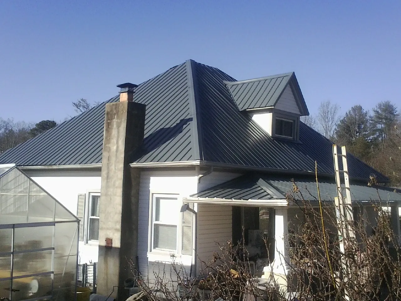 Dark blue standing seam metal roof on a white farmhouse with dormer — Slate & Tile Roof Repair by Roofing Brothers in Poncha Springs