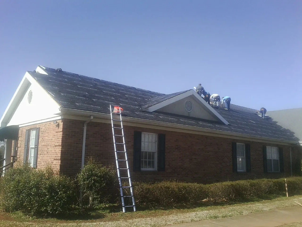 Crew tearing shingles off a brick ranch roof with a ladder set — Metal Roof Repair work by our crew in Poncha Springs