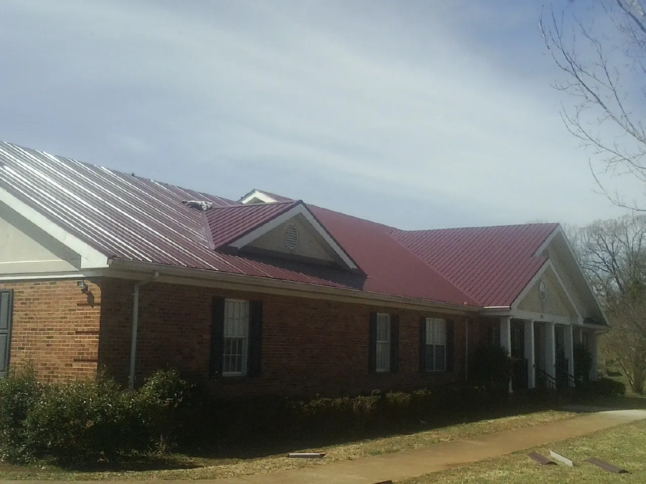Red metal roof with gabled entries on a long brick building, from a Hail Damage Roof Repair job in Poncha Springs