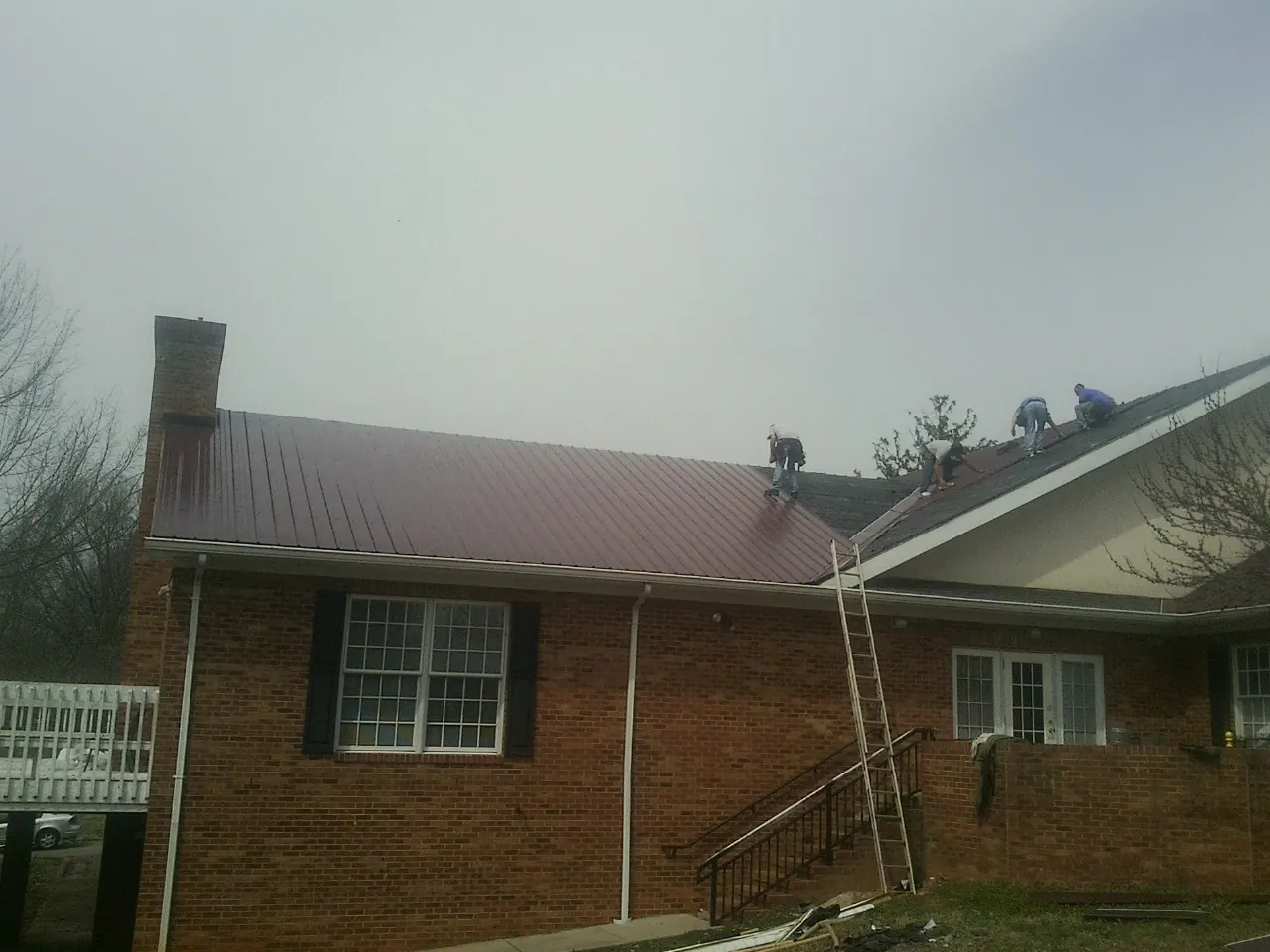 Crew setting red metal roofing panels on a brick home in Poncha Springs