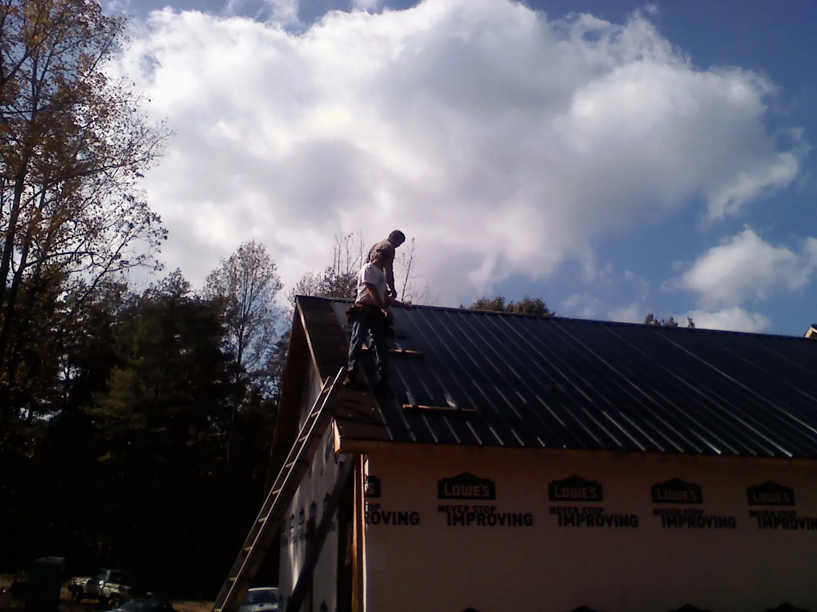 Roofer fastening dark metal panels high against a cloudy sky, from a Roof Inspection job in Poncha Springs