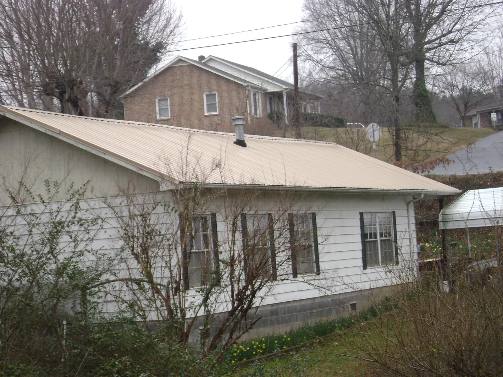 Tan metal roof on a white sided house set into a hillside — Commercial Roofing by Roofing Brothers in Poncha Springs